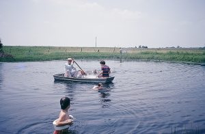 Farm - the pond - Swimming with ski belts, rowing the rowboat. The rowboat was very light, made of aluminum. We could carry or drag it down from where we kept it in the carport. We would use it to going. We always had fishing poles, and we would dig up worms in the garden to use for bait. These were some neighbors and guests joining us for some water recreation during their visit.