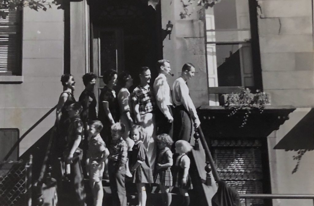 Family and friends are lined up by height, standing on the front stoop of the Pancoast’ house on Henry Street, directly across the street from our house.