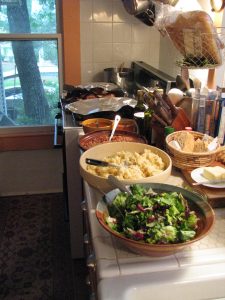 The kitchen counter ran all the way across from the stove to the shelves at the end, with the sink in the middle. There was plenty of space for serving bowls for buffet-style dinner parties. Through the window you can see out to the patio past the tree.