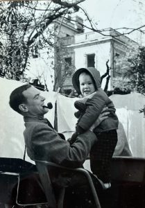 Italy - Rome - Clovis with a pipe in his mouth, holding Mary Elizabeth who is wearing a bonnet. They are in the back yard of our house in Via Bellotti Bon.